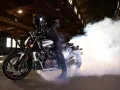 Motocyklista w kasku na Yamasze V-Max wykonuje burnout, tworząc kłęby dymu w opuszczonej hali.