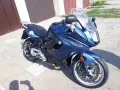 Błękitny motocykl BMW F800 GT stoi na chodniku przed garażem.