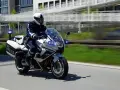 Policyjny motocykl BMW F800GT z włączonymi sygnałami świetlnymi pędzi po drodze.