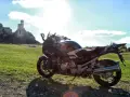 Motocykl na tle zamku na skale i zielonej łąki.