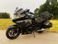 Czarny motocykl BMW K1600 Grand America z kuframi, gotowy na daleką podróż pośród zielonych pól i drzew.