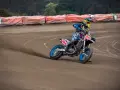 Motocyklista w kolorowym stroju śmiga po piaszczystym torze **flat track**, pochylony w zakręcie.