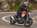 Motocyklista w kasku jedzie czerwonym motocyklem po krętej drodze. Idealny motor na początek przygody z jazdą.