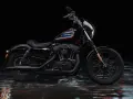 Czarny Harley-Davidson Iron 1200 z kolorowym paskiem na baku, stojący na mokrej, błyszczącej nawierzchni.