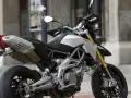 Srebrno-czarny motocykl Aprilia Dorsoduro 750 z żółtymi lagami, gotowy do jazdy po miejskich ulicach.