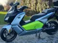 Srebrno-czarny skuter elektryczny BMW C Evolution z zielonym akcentem i napisem "C Evolution" na boku, stojący na chodniku.
