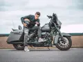 Mężczyzna w czarnej kurtce i podartych jeansach siedzi na motocyklu Harley-Davidson Street Glide, trzymając kask.
