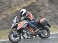 Motocyklista w kasku i kombinezonie śmiga na KTM Super Duke 1290 GT w deszczu.