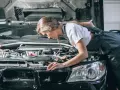 Młoda mechaniczka pochyla się nad silnikiem, sprawdzając go. To może być początek jej drogi, jak otworzyć warsztat samochodowy.