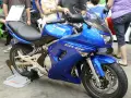Błękitny motocykl Kawasaki ER-6f, z widocznymi danymi technicznymi na owiewce, prezentowany na wystawie.