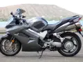 Szary motocykl Honda VFR 800 z widokiem na wodę i wzgórza w tle.
