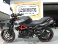 Czarny motocykl Aprilia Shiver 900 z czerwonym stelażem, zaparkowany przed salonem motocyklowym.
