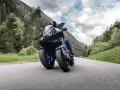 Motocyklista na Yamaha Niken pokonuje górską drogę, otoczony zielonymi lasami i skalistymi szczytami.