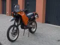 Pomarańczowy motocykl KTM 640 Adventure stoi na brukowanym podjeździe przed garażami.