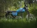 Niebieski motocykl MZ ETZ 250 stojący na trawie, z drzewami w tle.