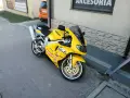 Żółty motocykl Suzuki TL1000R z naklejkami sponsorów, zaparkowany na chodniku.