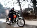 Mężczyzna w kasku i goglach pędzi na pomarańczowym motocyklu WSK 125. Widać dym z rury wydechowej, sugerujący dużą prędkość maksymalną.