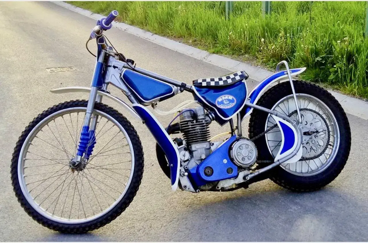 Niebieski motor żużlowy na asfalcie. Zastanawiasz się, ile kosztuje motor żużlowy? Ten wygląda na gotowy do startu!