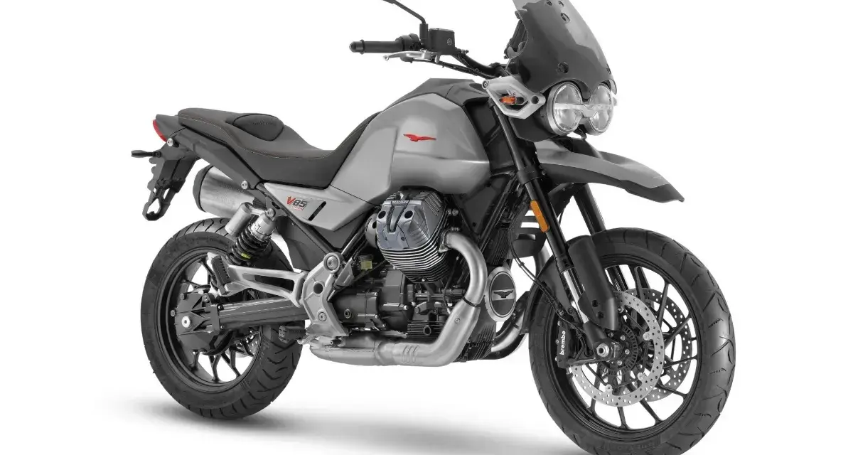Srebrny motocykl Moto Guzzi V85 TT z czarnym siedzeniem i przyciemnianą szybą, gotowy na przygodę.
