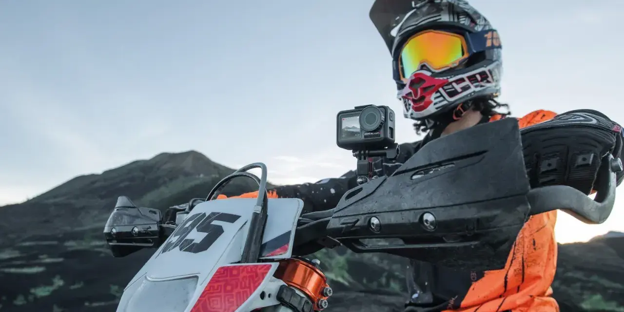 Motocyklista w kasku z kamerą na kierownicy, gotowy do jazdy po górskim terenie. Idealna kamera na kask motocyklowy do uchwycenia przygody.