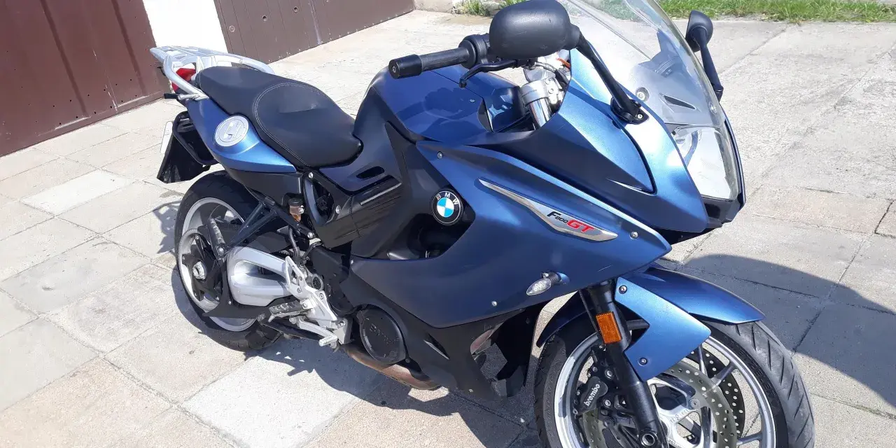 Błękitny motocykl BMW F800 GT stoi na chodniku przed garażem.