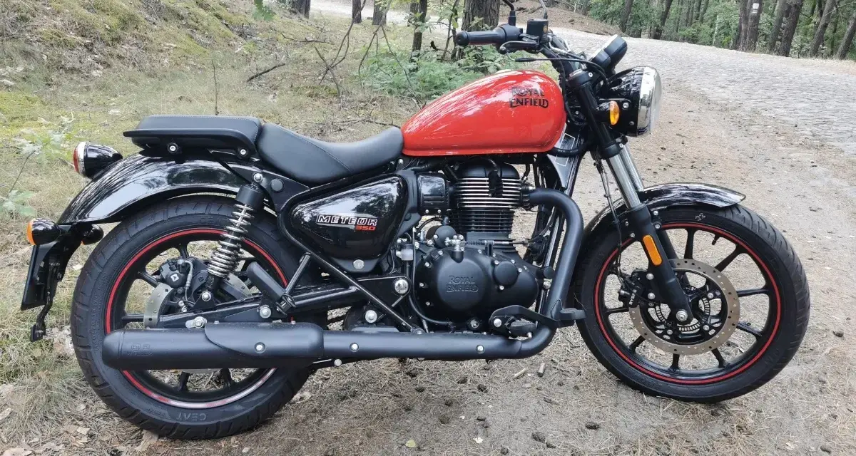 Czerwony Royal Enfield Meteor 350 na leśnej drodze. Klasyczny wygląd i nowoczesna technologia w jednym.