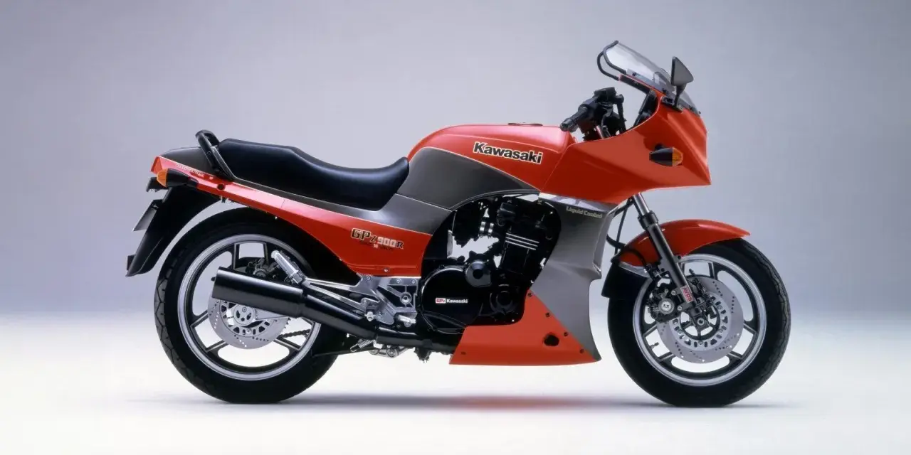 Pomarańczowy motocykl Kawasaki GPZ900R z szarymi akcentami, z lat 80., z owiewką i sportowym wyglądem.