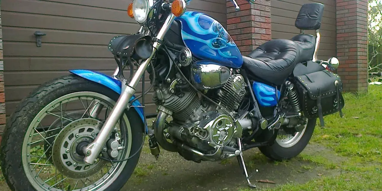 Błękitny motocykl Yamaha Virago 1100 z płomieniami, skórzanymi sakwami i oparciem. Wady i zalety tego klasyka do rozważenia przed zakupem.