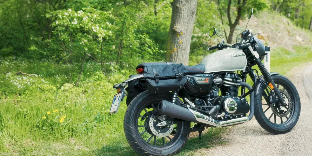 Stojący na poboczu, w otoczeniu zieleni, motocykl Honda GB350 z sakwami gotowy na podróż.
