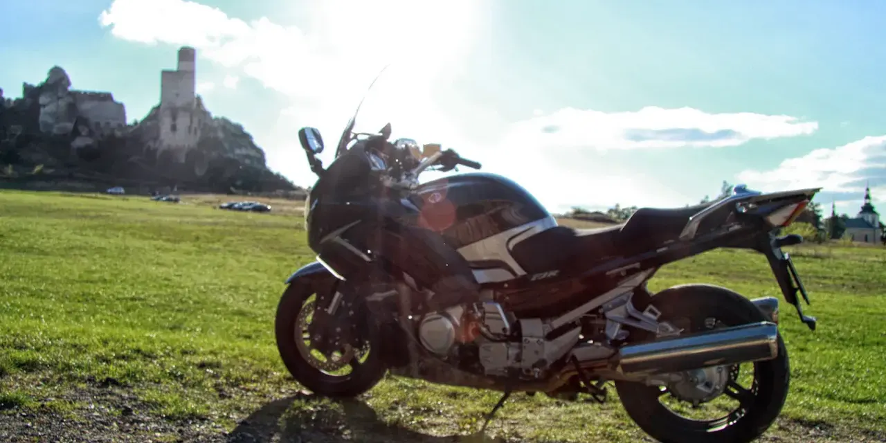 Motocykl na tle zamku na skale i zielonej łąki.
