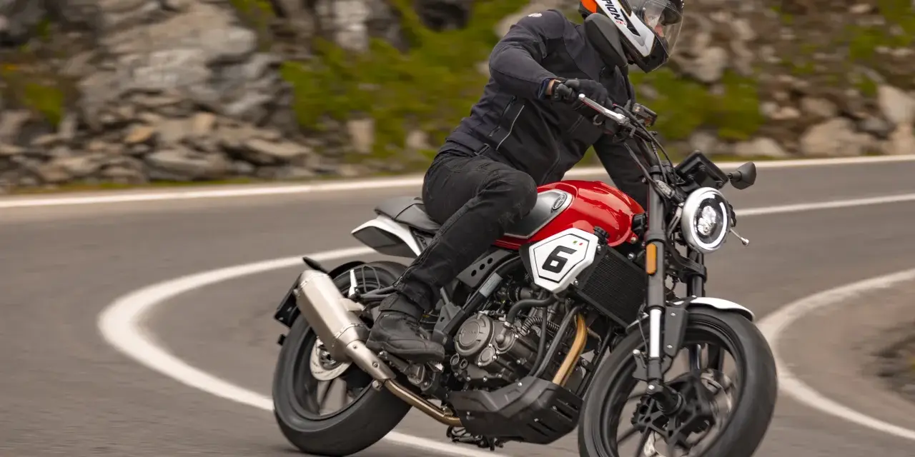 Motocyklista w kasku jedzie czerwonym motocyklem po krętej drodze. Idealny motor na początek przygody z jazdą.