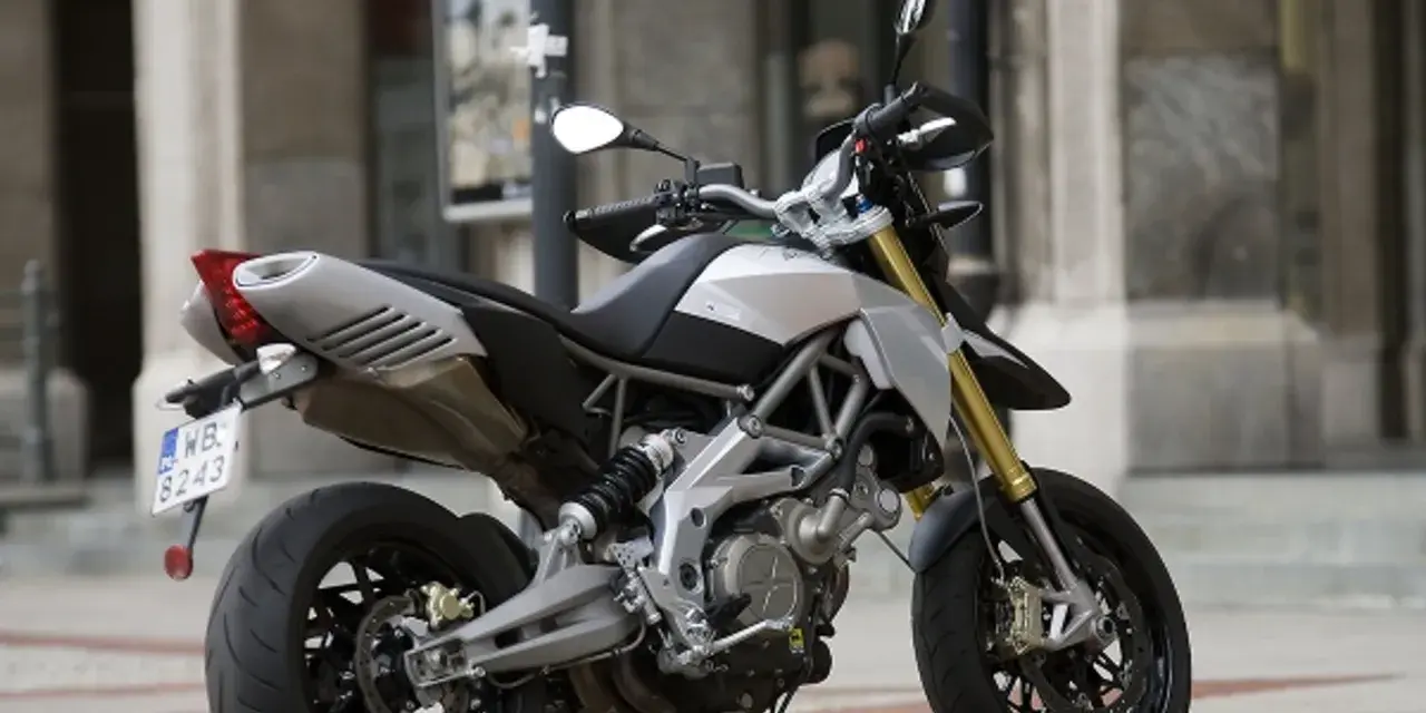Srebrno-czarny motocykl Aprilia Dorsoduro 750 z żółtymi lagami, gotowy do jazdy po miejskich ulicach.