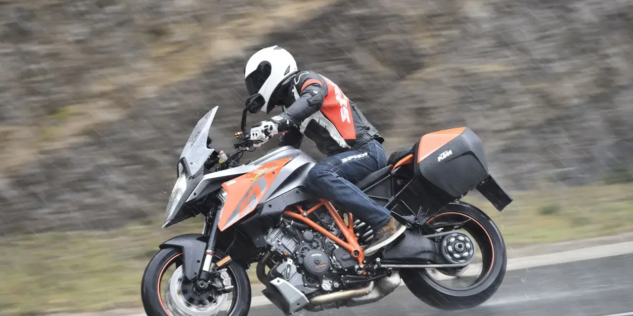 Motocyklista w kasku i kombinezonie śmiga na KTM Super Duke 1290 GT w deszczu.