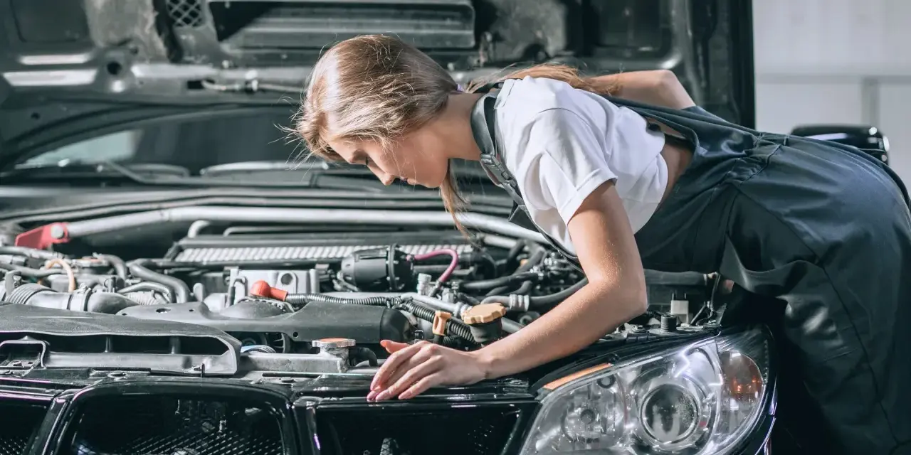 Młoda mechaniczka pochyla się nad silnikiem, sprawdzając go. To może być początek jej drogi, jak otworzyć warsztat samochodowy.