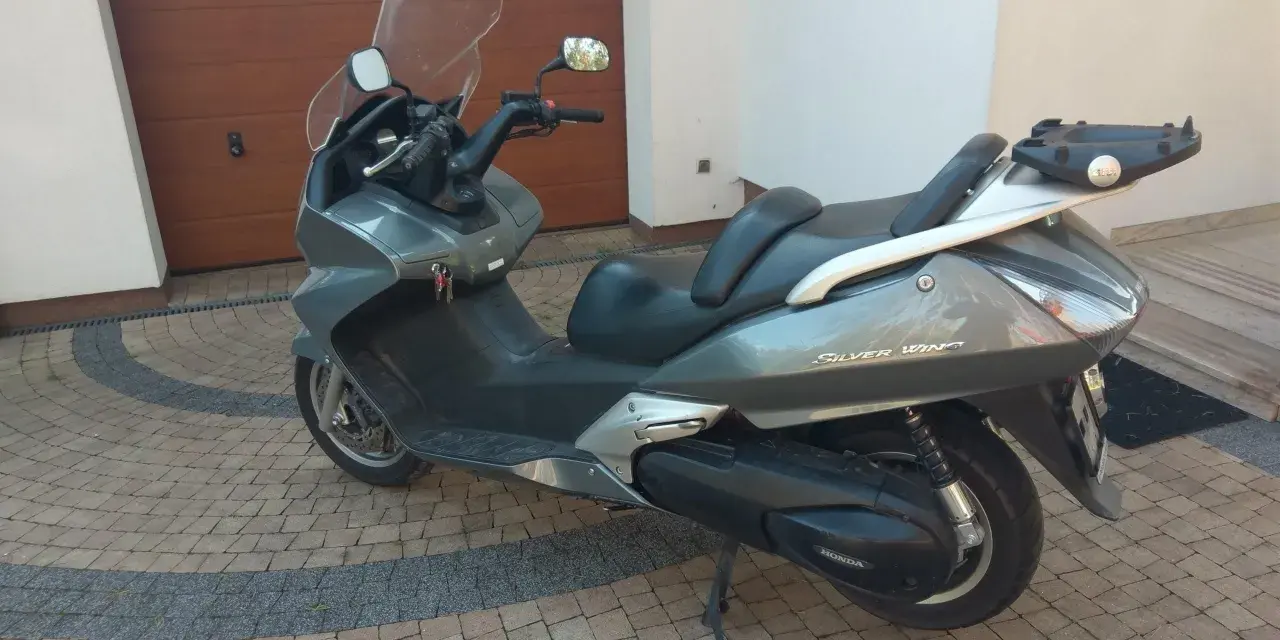 Szary skuter Honda Silver Wing 600 stoi na kostce brukowej przed garażem.