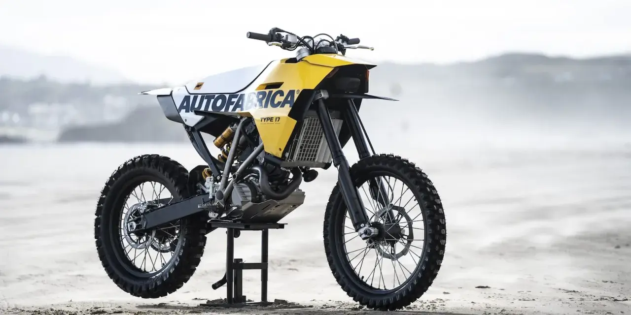 Żółto-biały motocykl customowy Autofabrica Type 17, bazujący na BMW G450X, stoi na plaży.
