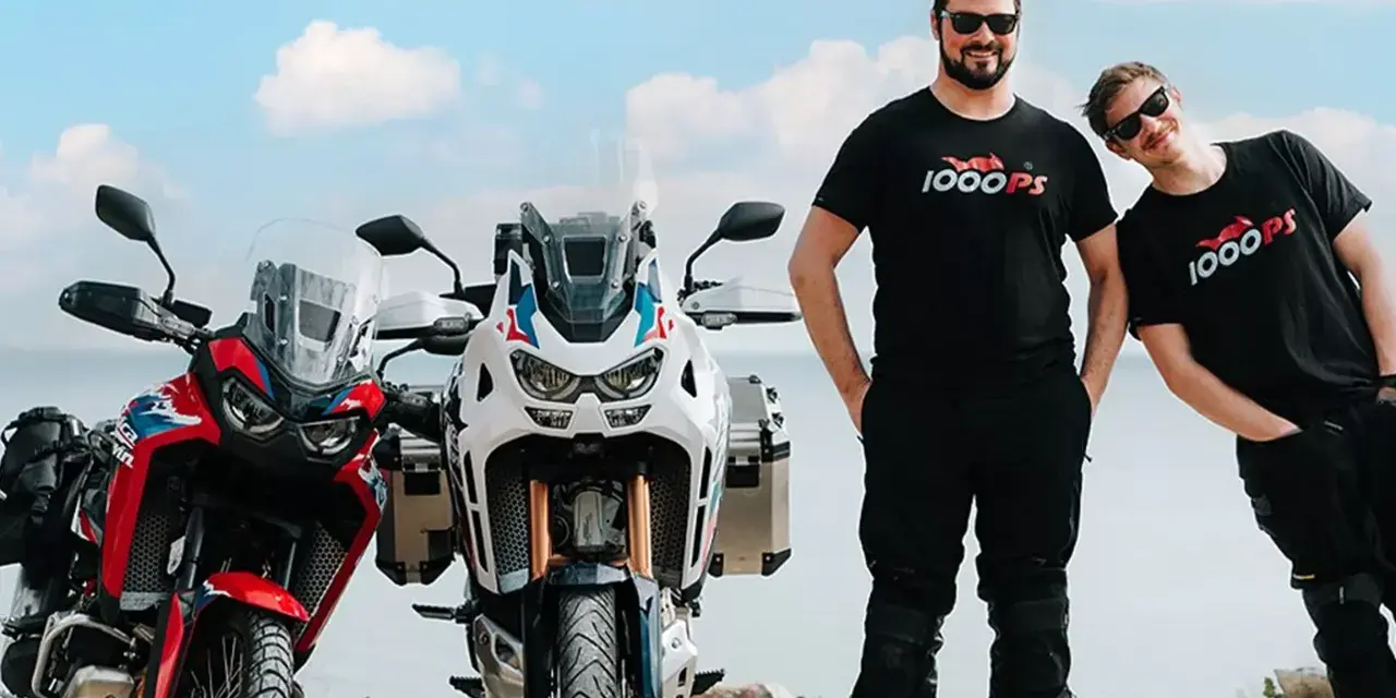Dwóch mężczyzn w koszulkach 1000PS obok motocykli Honda Africa Twin.