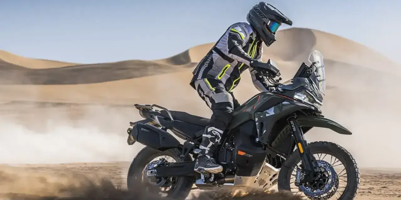 Motocyklista w pełnym rynsztunku szaleje na pustyni na swoim KTM 790 Adventure, wzbijając tumany piasku.