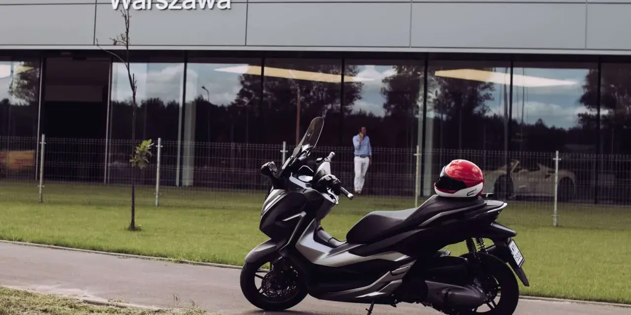 Elegancki skuter Honda Forza 300 zaparkowany przed budynkiem z napisem "Warszawa". Czerwony kask leży na siedzeniu.