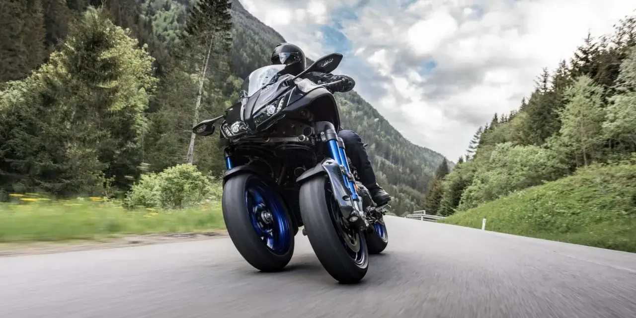 Motocyklista na Yamaha Niken pokonuje górską drogę, otoczony zielonymi lasami i skalistymi szczytami.