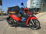 Czerwony Piaggio Liberty 125, obok niebieskiego, na tle miasta. Idealny do sprawdzenia piaggio liberty 125 dane techniczne.