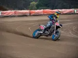 Motocyklista w kolorowym stroju śmiga po piaszczystym torze **flat track**, pochylony w zakręcie.