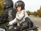 Uśmiechnięte dziecko na motocyklu, siedzące przed dorosłym, w kasku i kurtce motocyklowej.