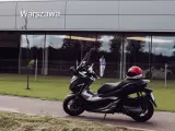 Elegancki skuter Honda Forza 300 zaparkowany przed budynkiem z napisem "Warszawa". Czerwony kask leży na siedzeniu.