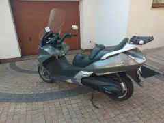 Szary skuter Honda Silver Wing 600 stoi na kostce brukowej przed garażem.