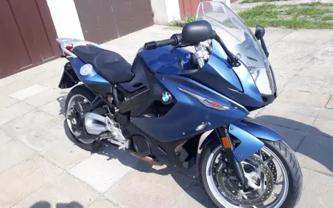 Błękitny motocykl BMW F800 GT stoi na chodniku przed garażem.