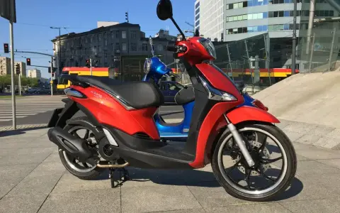 Czerwony Piaggio Liberty 125, obok niebieskiego, na tle miasta. Idealny do sprawdzenia piaggio liberty 125 dane techniczne.