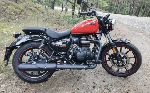 Czerwony Royal Enfield Meteor 350 na leśnej drodze. Klasyczny wygląd i nowoczesna technologia w jednym.