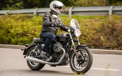 Motocyklista w kasku i skórzanej kurtce jedzie na stylowym motocyklu Moto Guzzi V9.