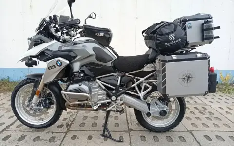 Srebrny motocykl BMW R1200GS z kuframi i torbą na bak. Wady tego modelu to m.in. wysoka cena i skomplikowana elektronika.